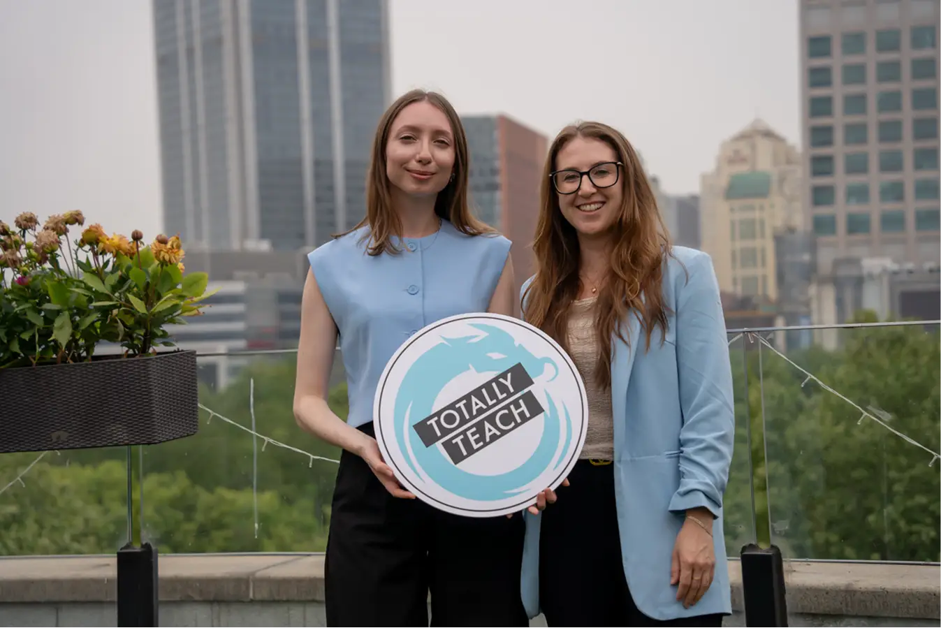 Rose and Rowena holding a Totally Teach sign on a city rooftop